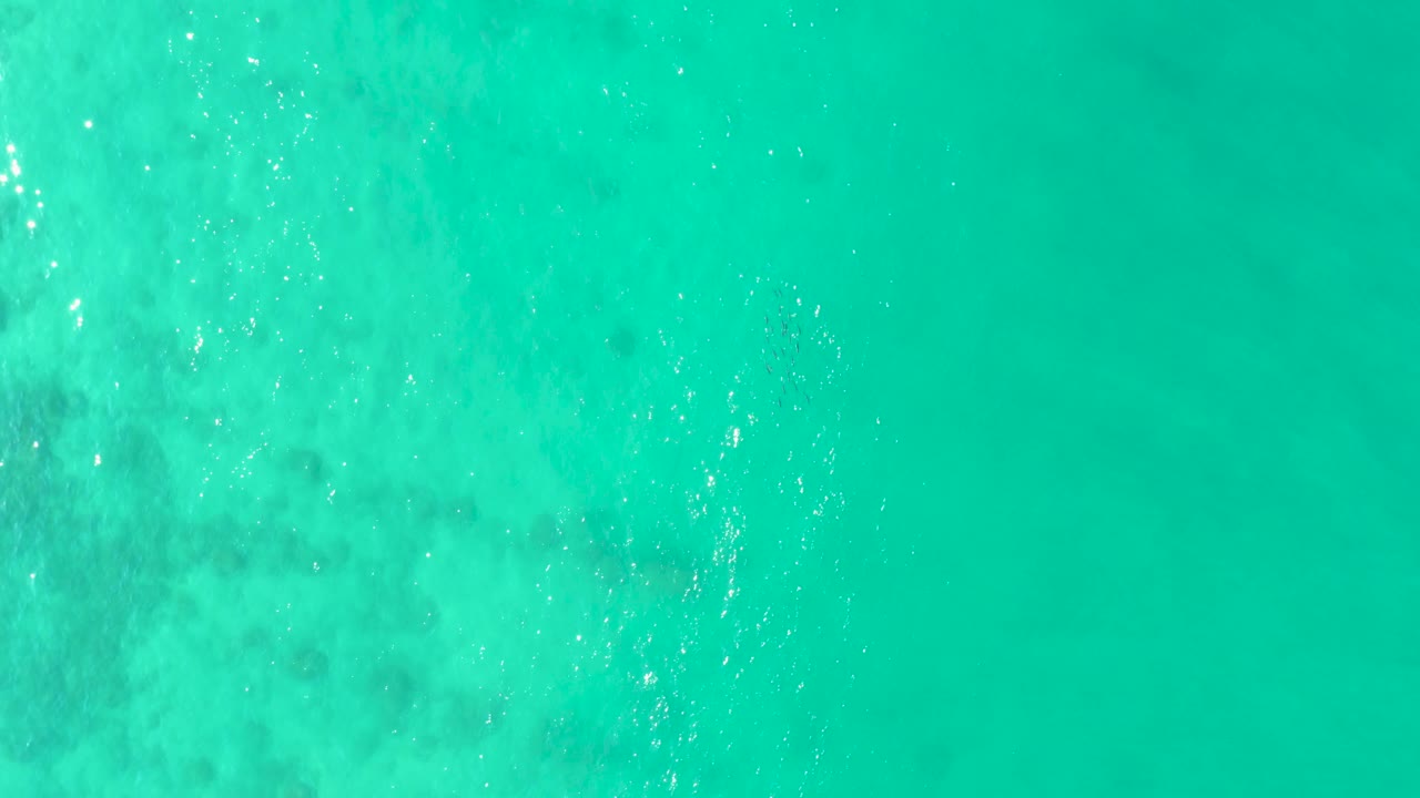 Aerial view of turquoise ocean at Los Frailes with a vertical band of bright sun glitter near the right side and no visible people.