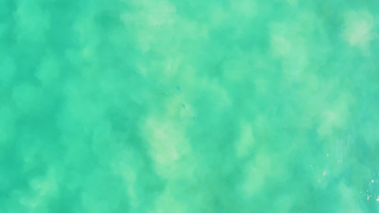 An overhead view of mottled turquoise water at Los Frailes shows seabed texture and shifting light patterns, with no visible people.