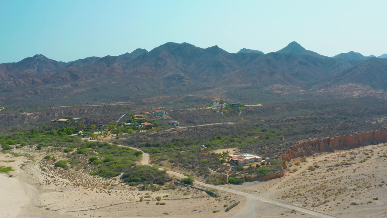 High desert landscape with road, brush, buildings, and mountains.