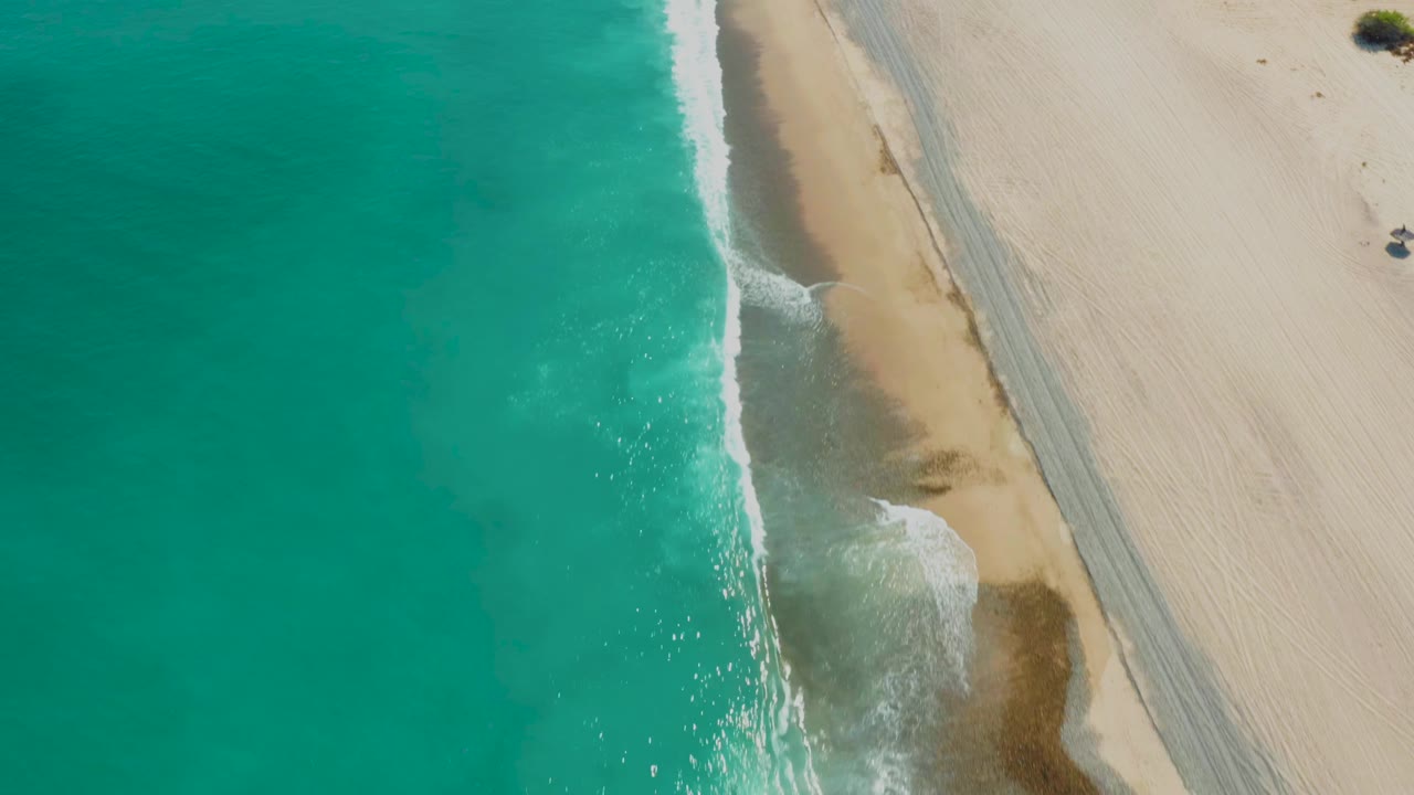 Aerial frame over Los Frailes with the white wave edge curving along the sand while the beach track sits farther inland, with no visible people.