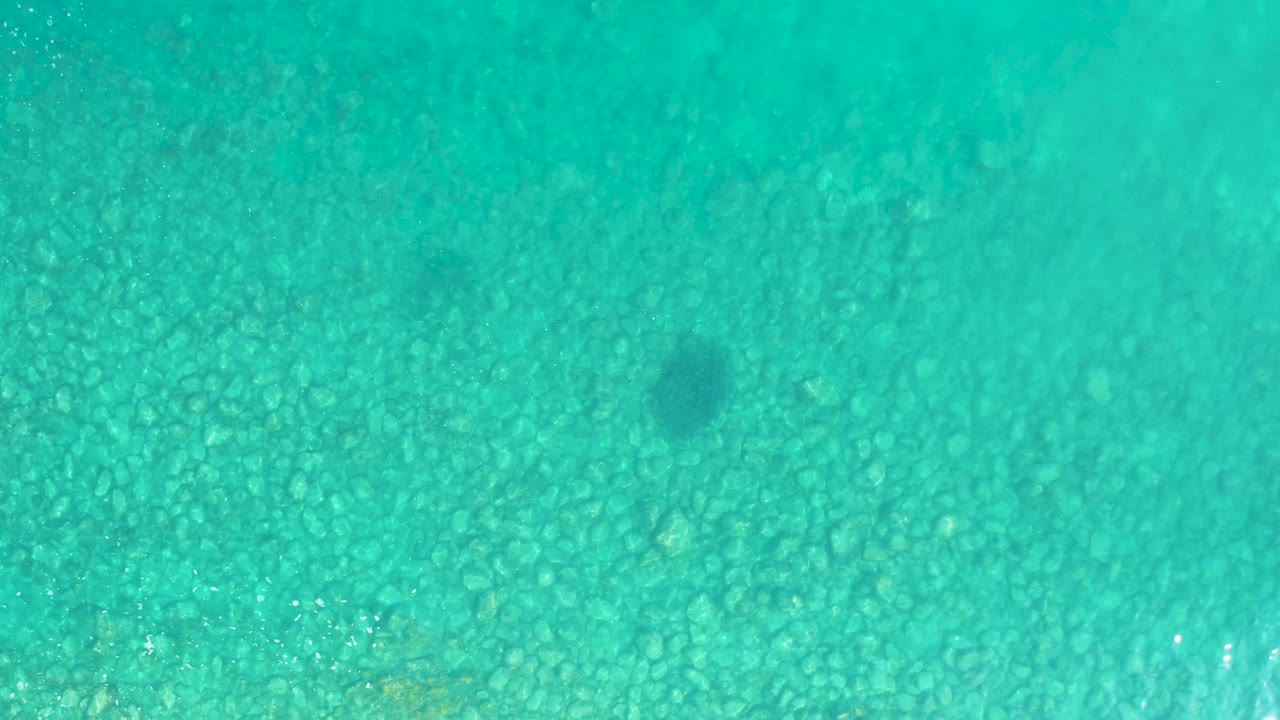 Rippled turquoise water covers the frame with the pebbly seabed visible underneath and no shoreline, boats, or people in view.