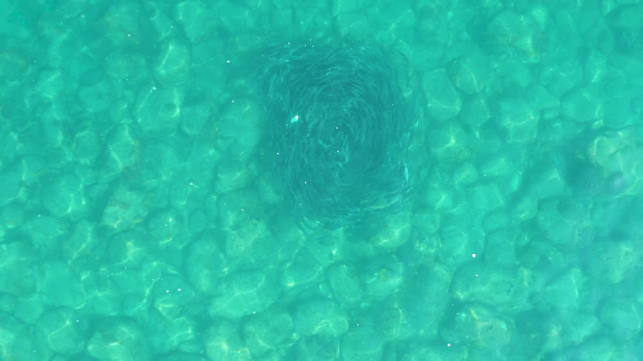 Clear turquoise water with stone-like bottom pattern and a dark shadow near the left side.