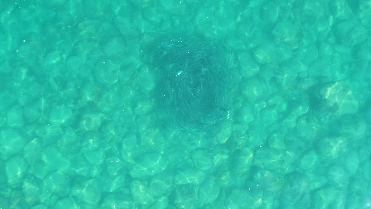 Overhead turquoise pool water in Los Frailes, Los Cabos shows a faint dark patch near the upper center over the patterned bottom, with no visible people.