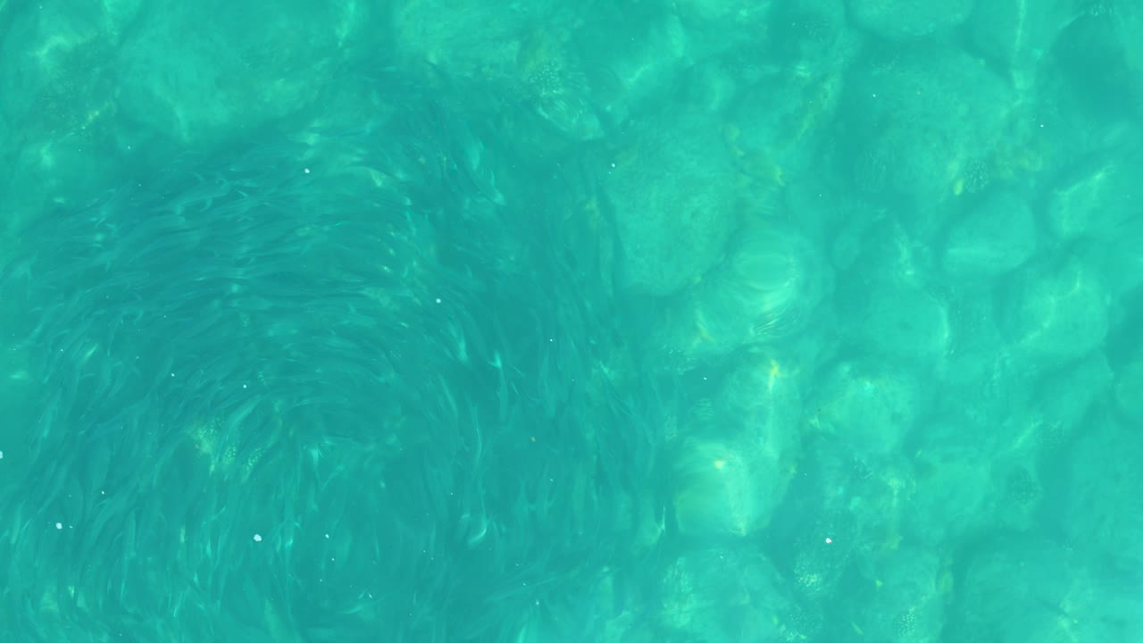 Top-down view of turquoise water over pale rocks at Los Frailes, Los Cabos, with soft ripples and no visible people.