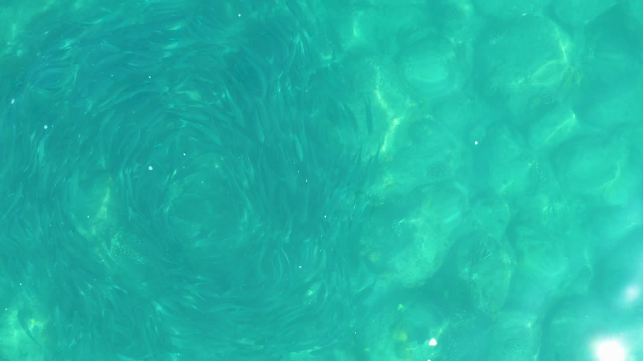 At 0:02, the rocky bottom remains visible through the turquoise surface while the darker vortex shape becomes more diffuse, with no visible people.