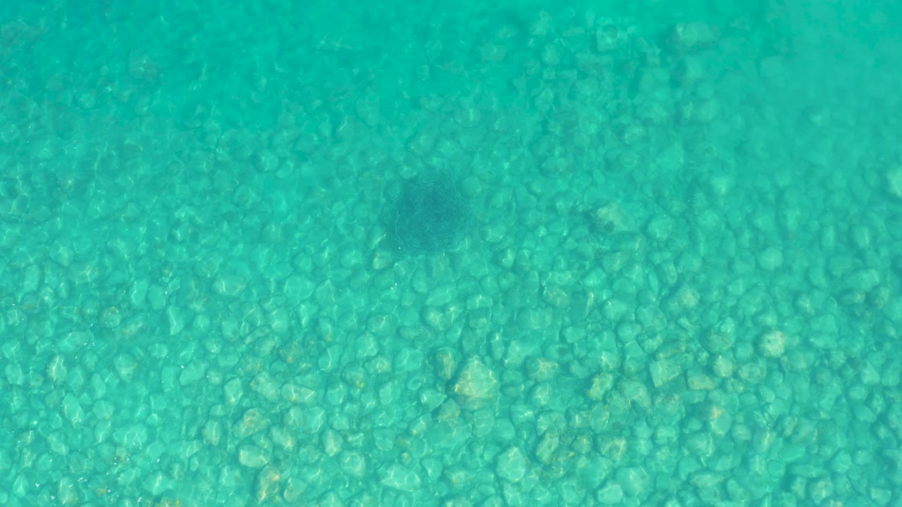 A slightly brighter patch of clear turquoise water crosses the stone seabed in Los Frailes, Los Cabos, with no visible people or objects above the water.