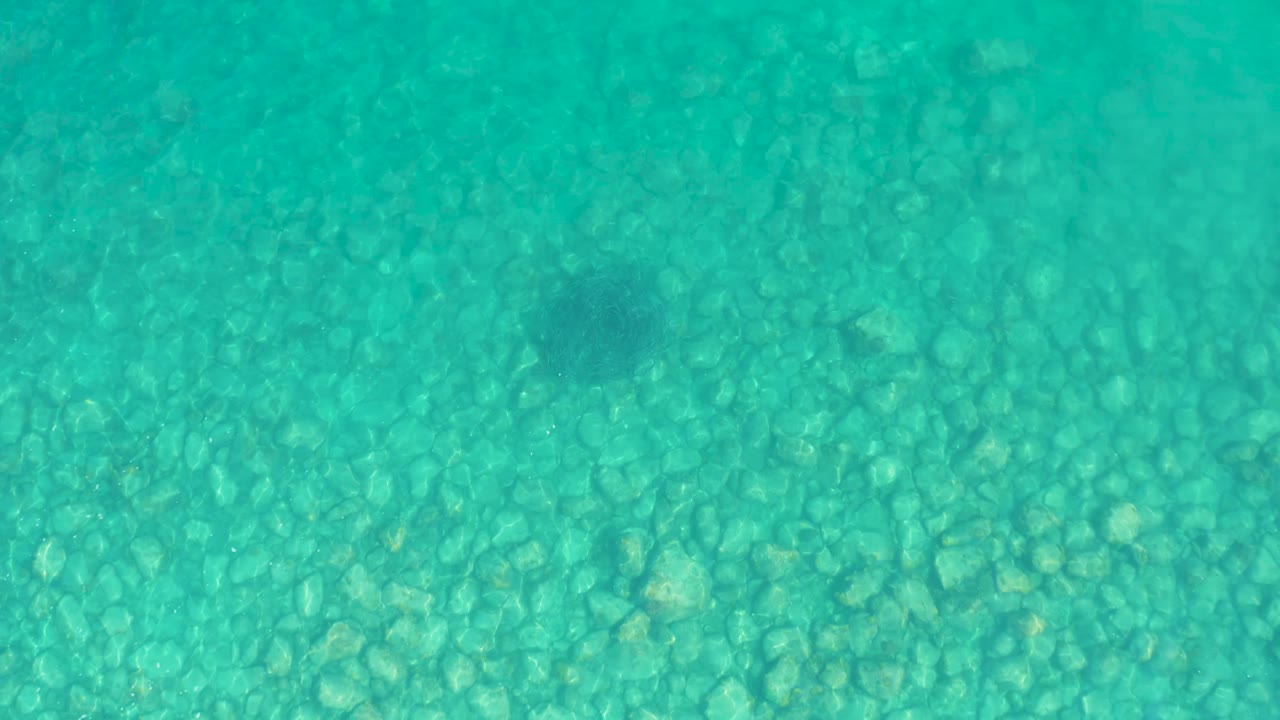 The pebbled ocean floor fills the frame under green-blue water in Los Frailes, Los Cabos, with soft light variation and no visible people.