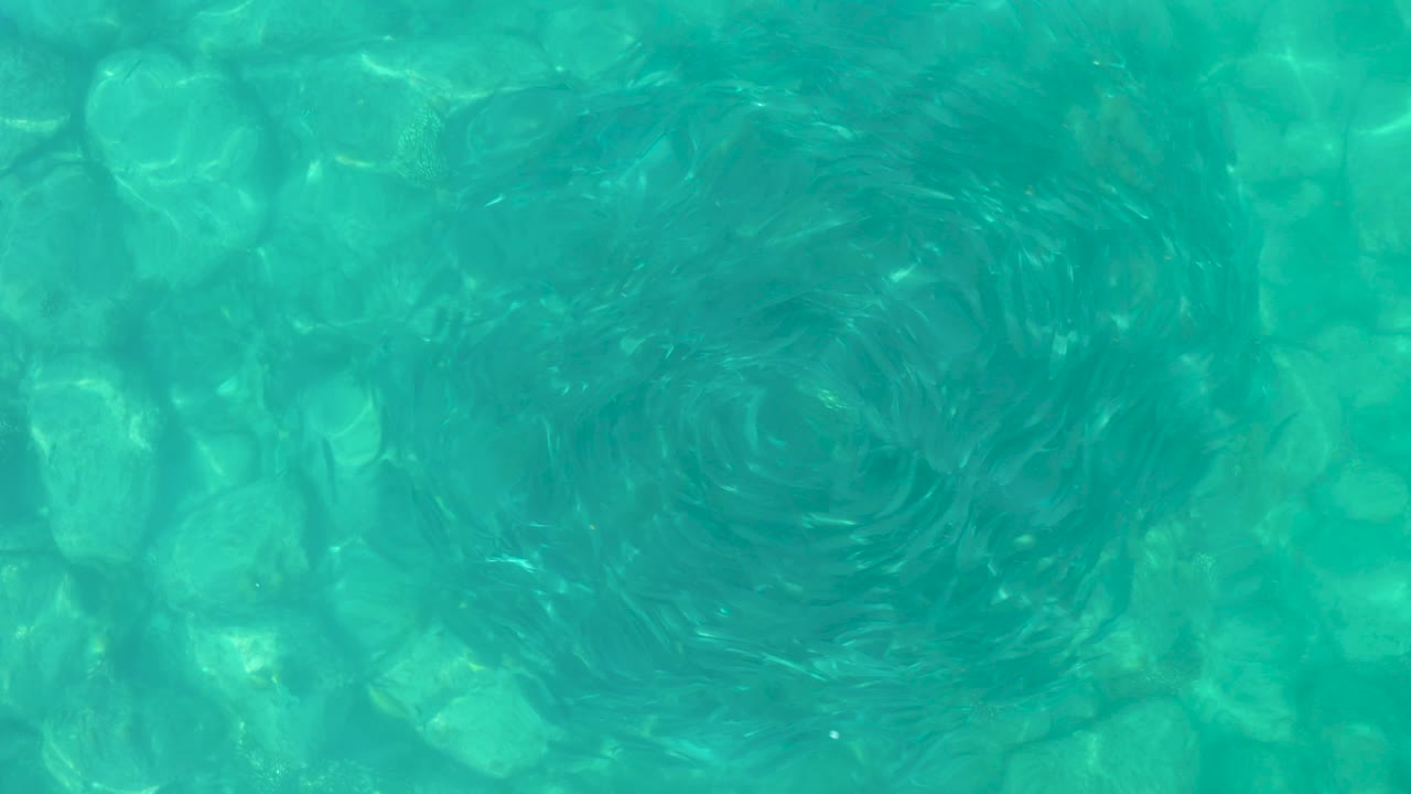 Los Frailes turquoise water fills the frame as the darker circular current shifts leftward over the rocky bottom, with no visible people or structures.