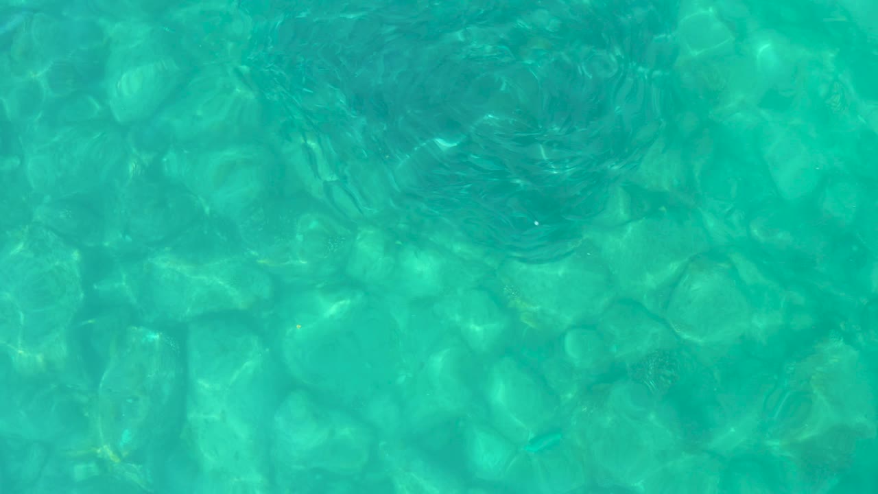 Clear blue-green water fills the frame in Los Frailes, with the rocky bottom softened by moving ripple patterns and no visible people.