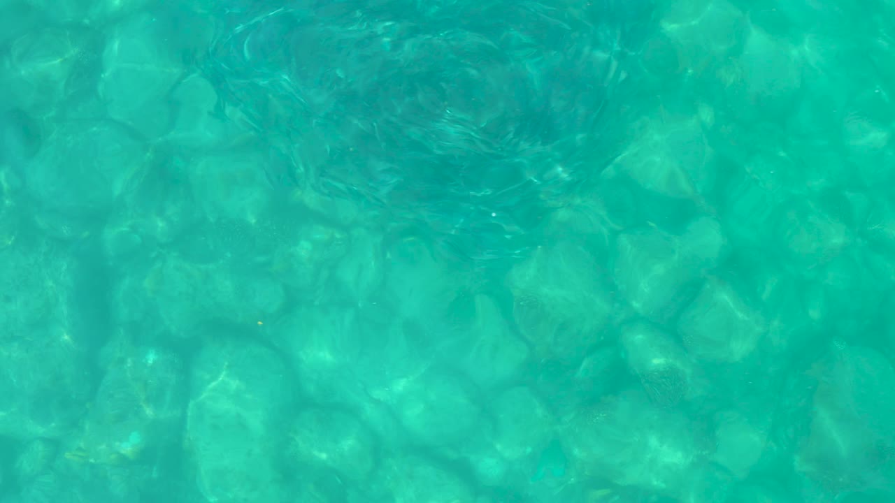 Shallow turquoise water in Baja California Sur shows darker ripple patches crossing over pale submerged rocks, with no visible people in frame.
