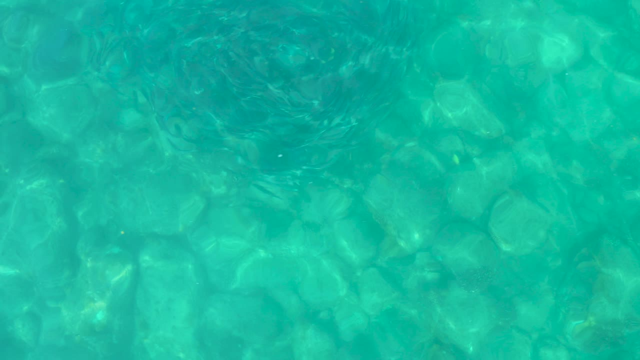 Transparent Los Frailes water reveals rounded stones beneath the surface, with small sun flecks and no visible people.