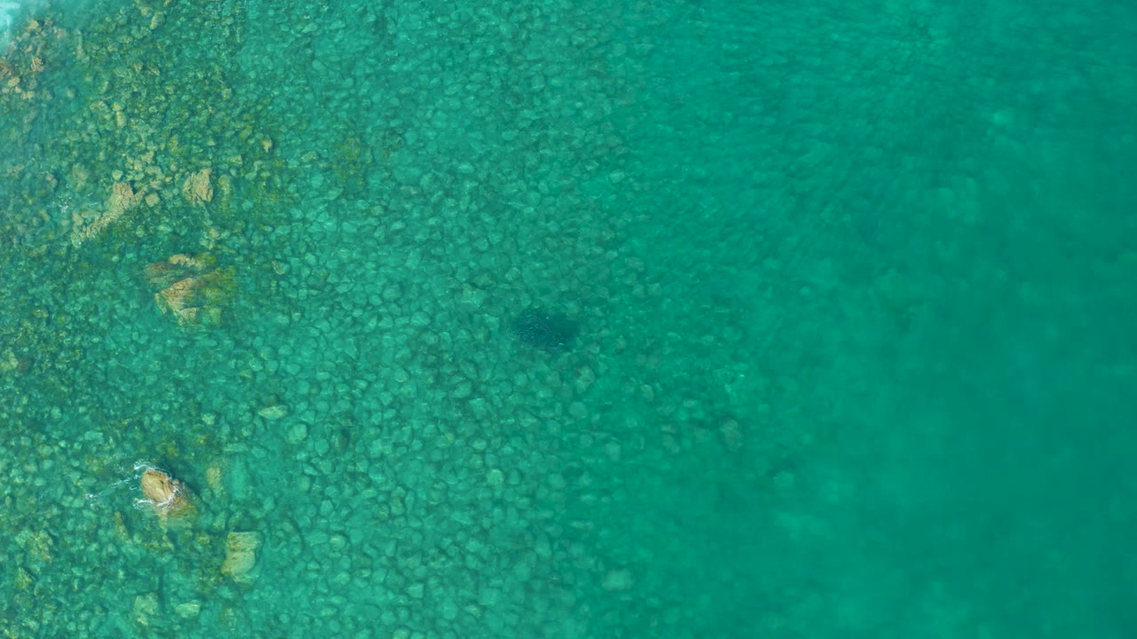 Turquoise shallow water over rocks with a small dark fish.