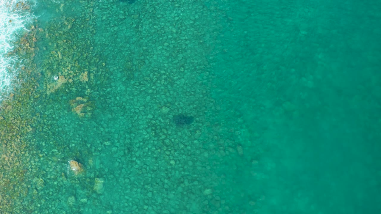 Rocky shallow seabed under turquoise water with foam on the left