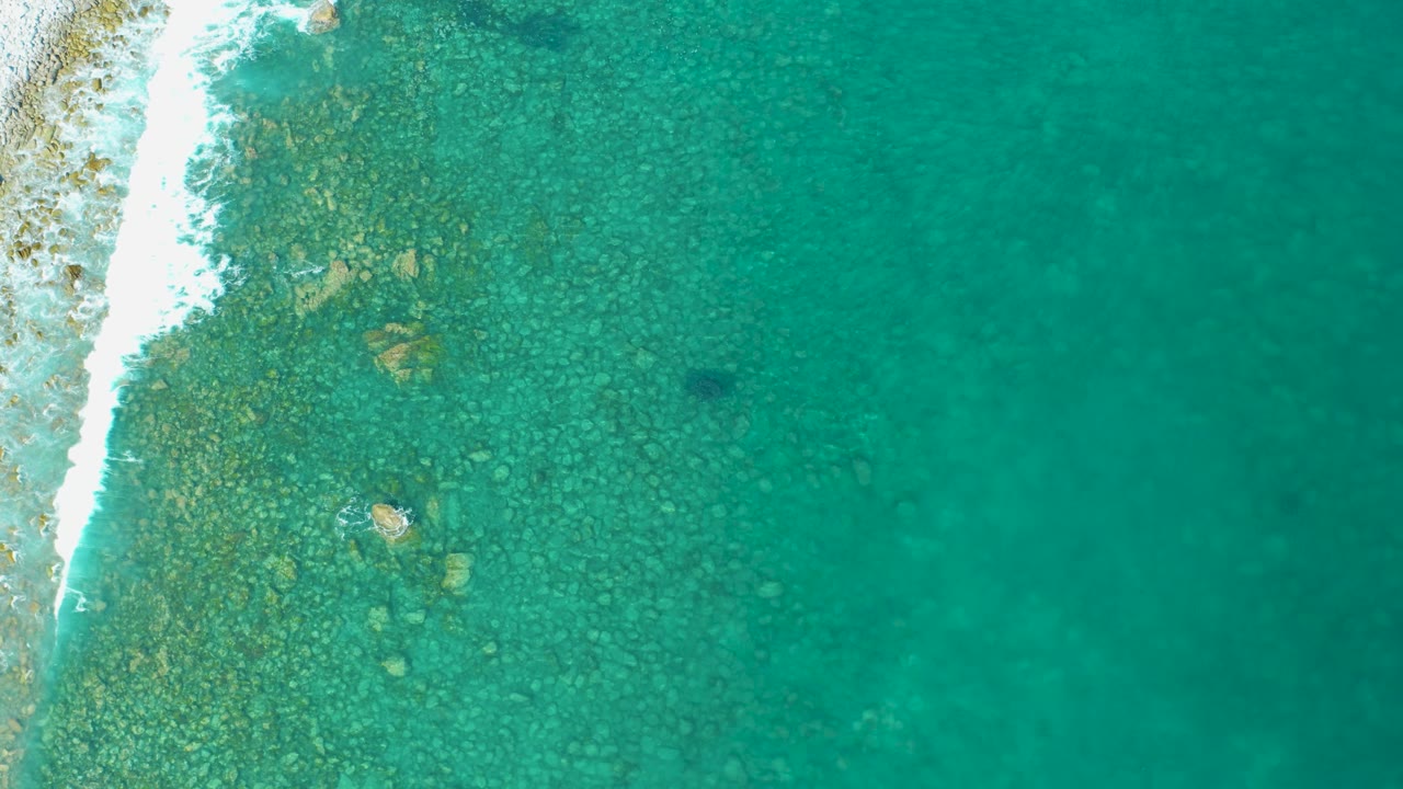 Clear shallow water over rocks with surf at left