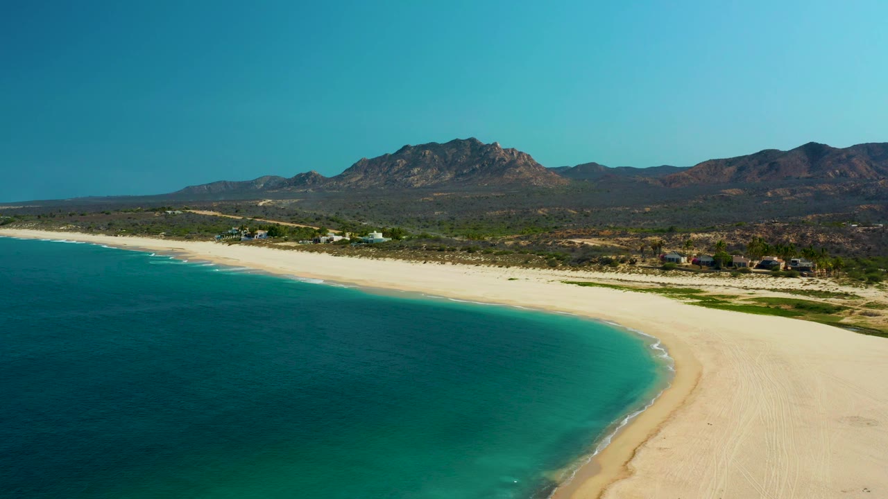 Turquoise water and sandy beach seen from above with desert mountains in the background.