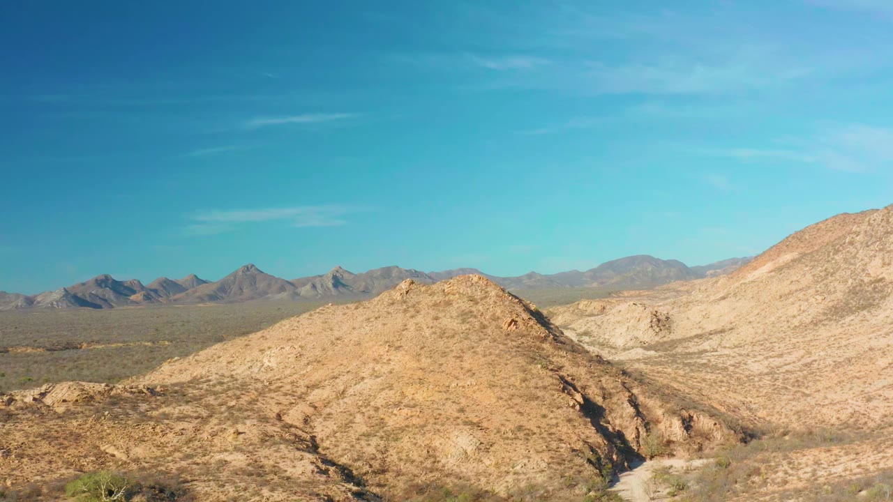 Rocky rounded hill dominates the center near Cabo Pulmo, Baja California Sur, with pale slopes to the right, distant mountains to the left, and no visible people.