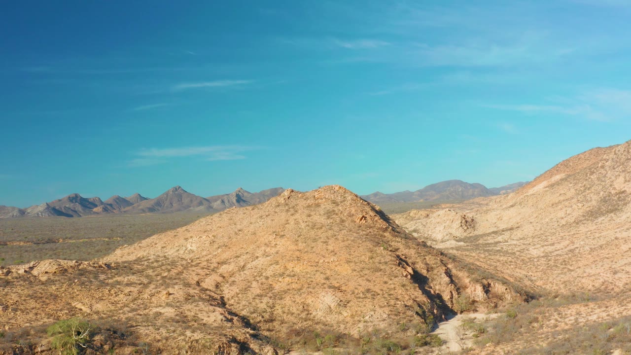 A wide Cabo Pulmo, Baja California Sur desert frame shows cactus and shrubs along the bottom, rocky hills across the middle, distant mountains, and no visible people.