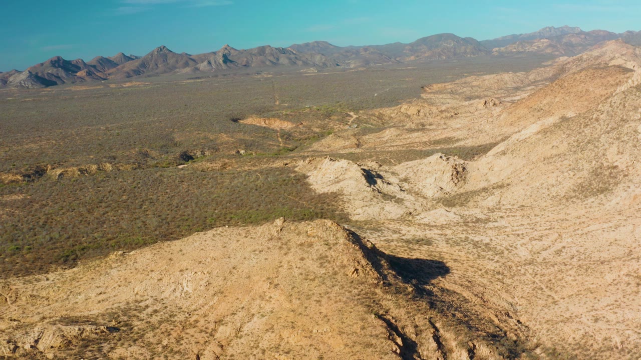 Aerial view of rocky desert hills and distant mountains under blue sky.