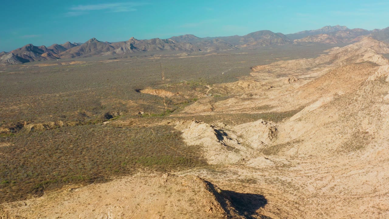 Elevated Cabo Pulmo desert view with a low sandy ridge in front, an arid scrubland valley beyond it, layered mountains in the distance, and no visible people.