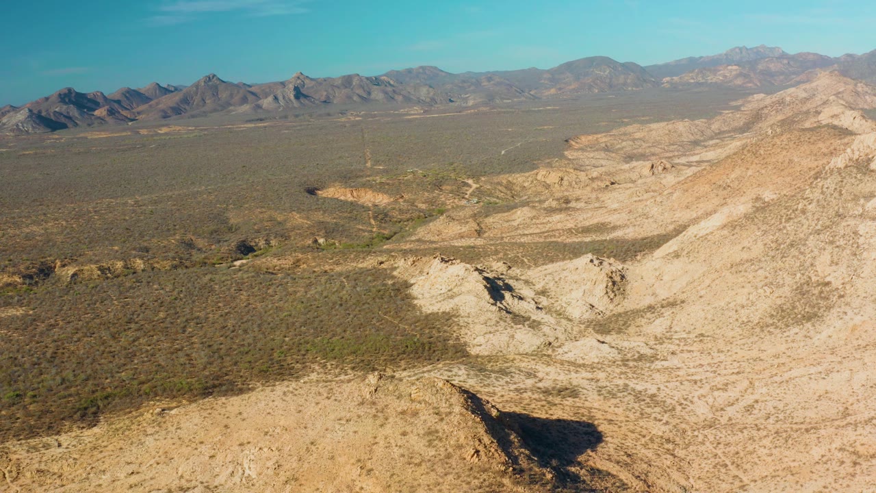 Aerial view in Cabo Pulmo looking across rocky desert hills and a wide dry valley toward a continuous mountain horizon, with no visible people.