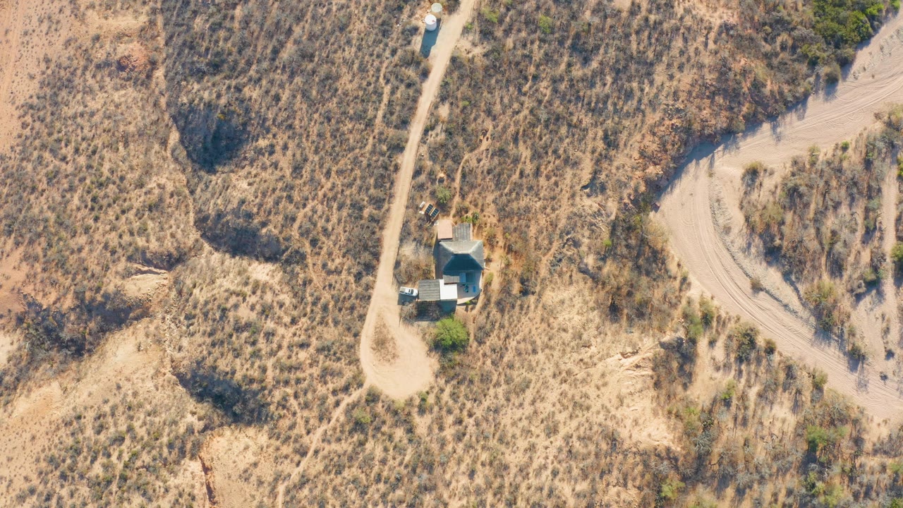 Aerial frame in Cabo Pulmo, Baja California Sur, with the vehicle slightly lower along the road near the small structure, surrounded by tan dry vegetation and no visible people.