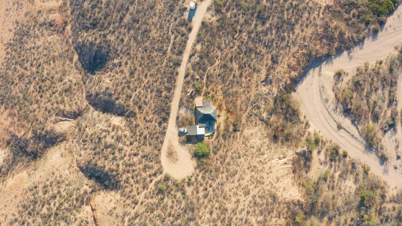 Overhead shot of a vehicle by a dirt track and small structure in dry terrain.