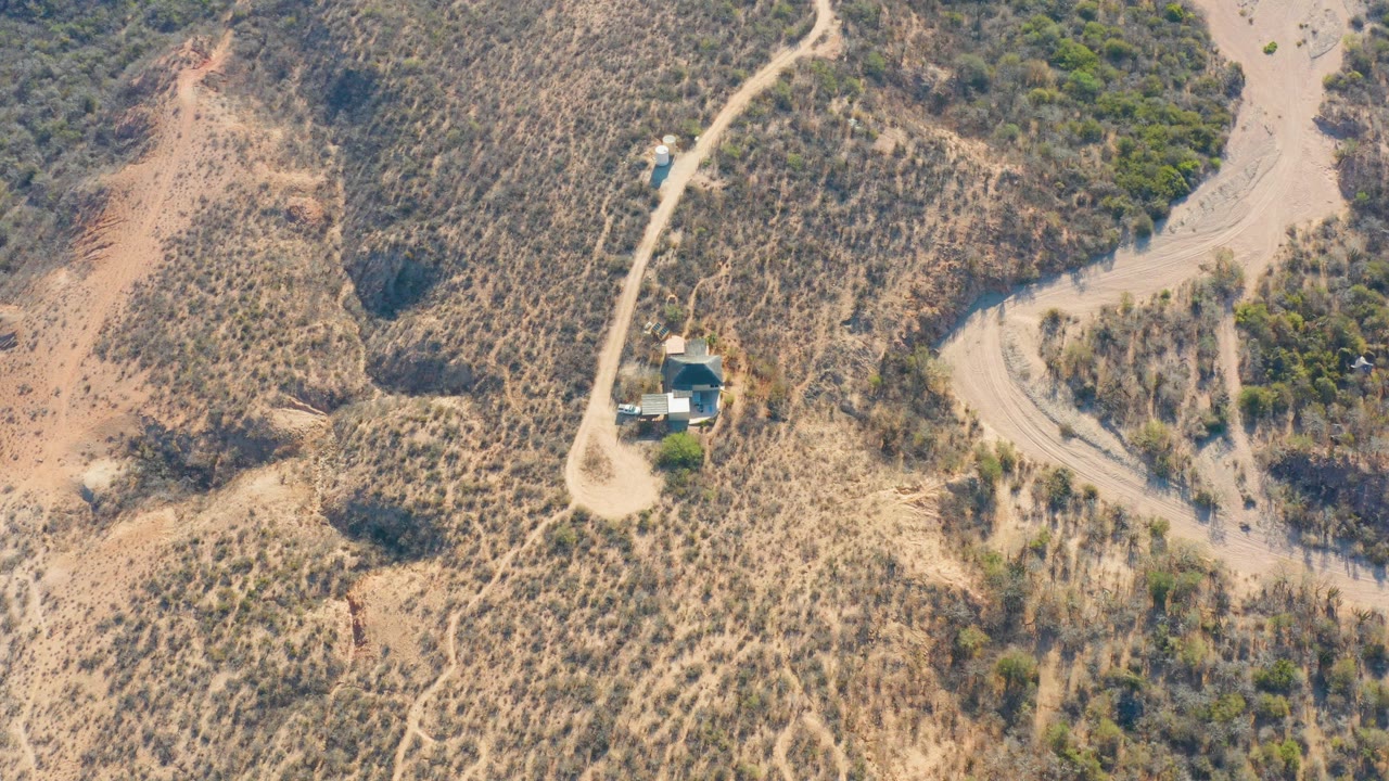 Aerial frame over Cabo Pulmo, Baja California Sur, showing a pale dirt road cutting through tan hillsides with scattered shrubs and no visible people.