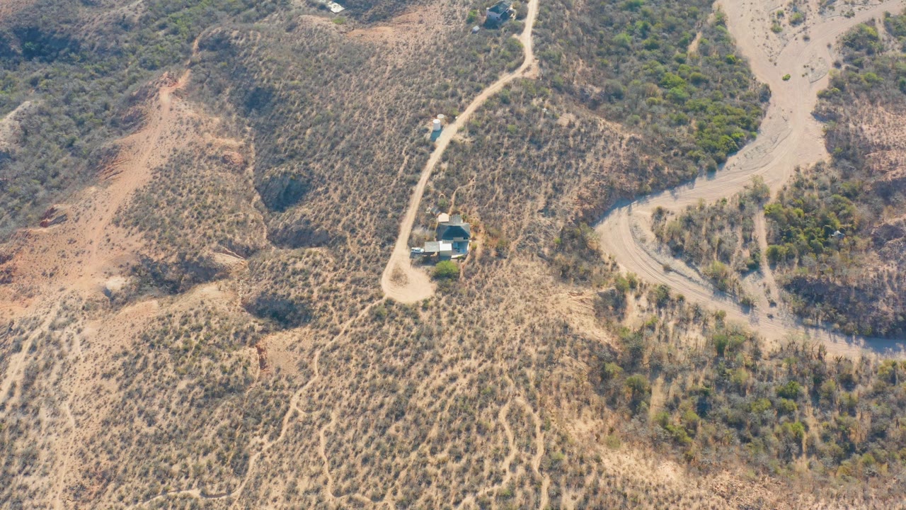 Dry hillside road curving past a small building and scrub vegetation.