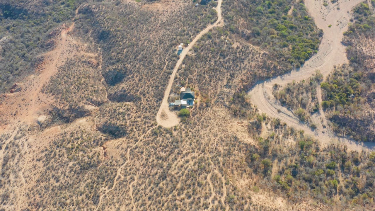 Aerial hillside road with a small building and branching dirt track.