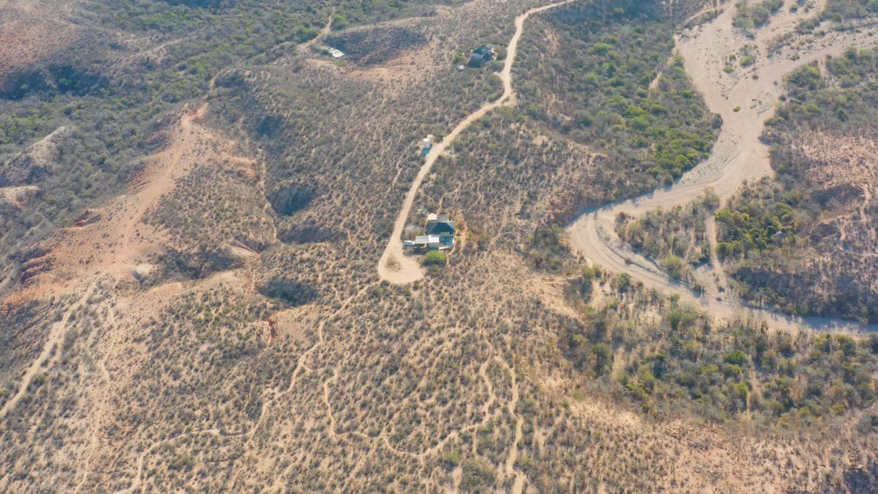 Aerial hillside landscape with a winding road, vehicle, and scrub vegetation.