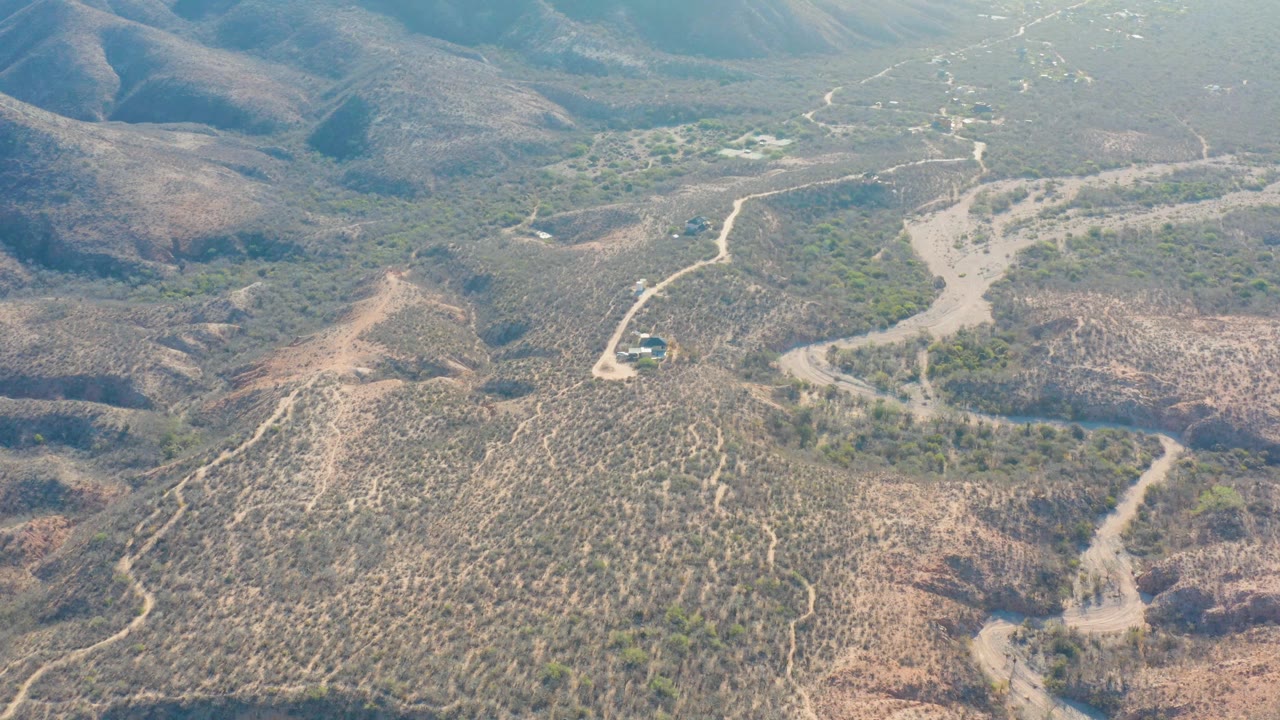 Elevated Cabo Pulmo view with the dirt road running from the lower frame toward a pale wash and distant hills, with no visible people.
