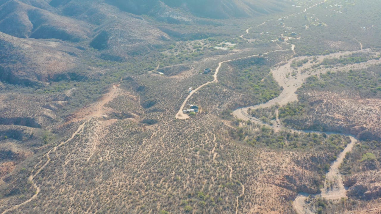 High aerial view in Cabo Pulmo with the pale road and wash crossing dry, scrub-covered hills, and no visible people.