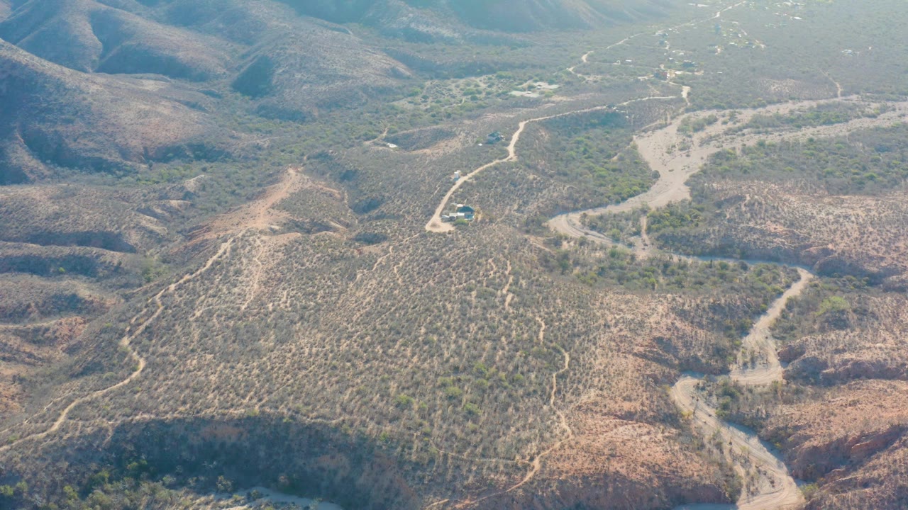 Cabo Pulmo aerial view with a pale road cutting through dry scrubland, low hills on both sides, a small vehicle near the road, and no visible people.