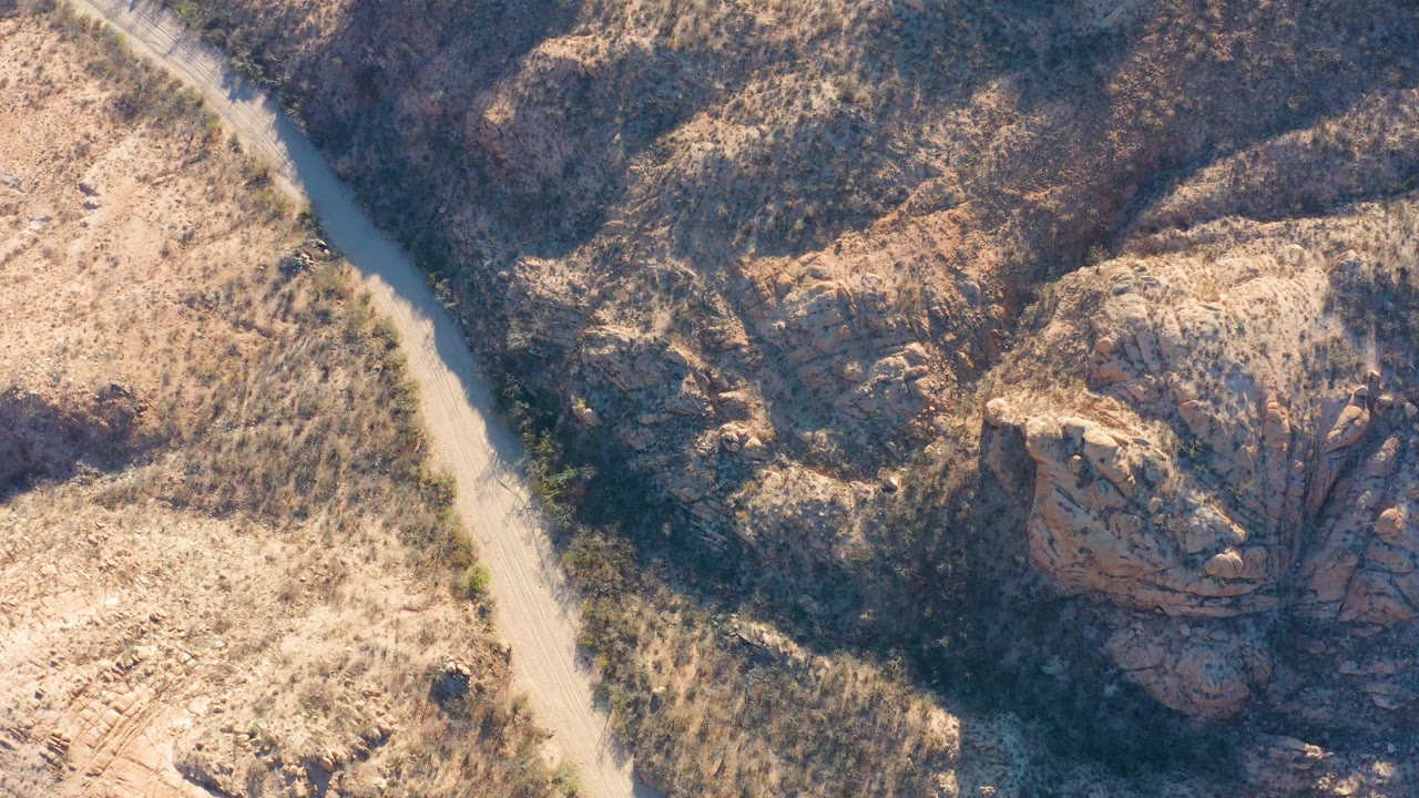 Aerial view of dirt road and rugged desert hillside.