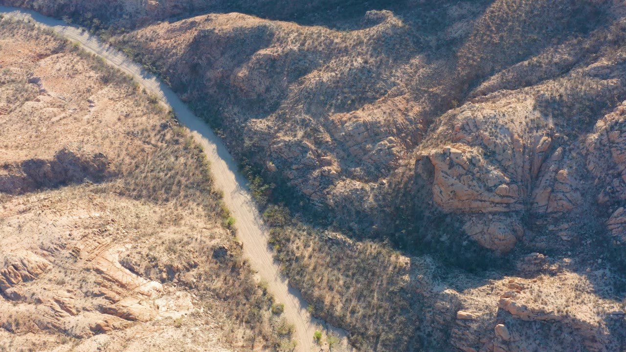 Aerial view of a pale winding road through rocky arid hills.
