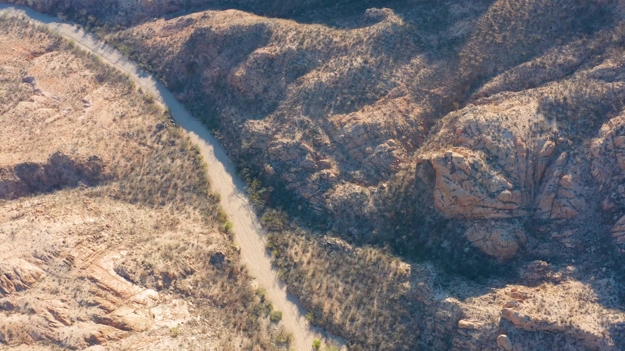 The Cabo Pulmo aerial view keeps the pale road on the left while layered rocky ridges fill the center and right, with no visible people.