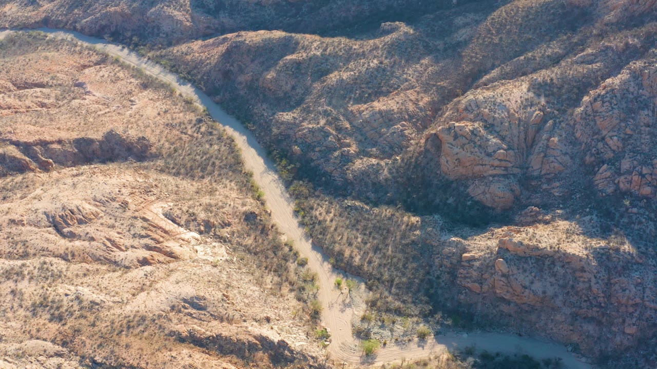 Aerial frame over Cabo Pulmo showing the river bend farther down the channel, with pale exposed rock on the left and darker rugged hills on the right, no visible people.