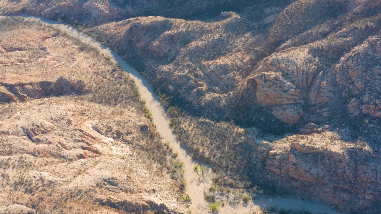 Aerial view in Cabo Pulmo, Baja California Sur, where a narrow blue-green river channel divides dry scrub and rounded rocky hills, no visible people.