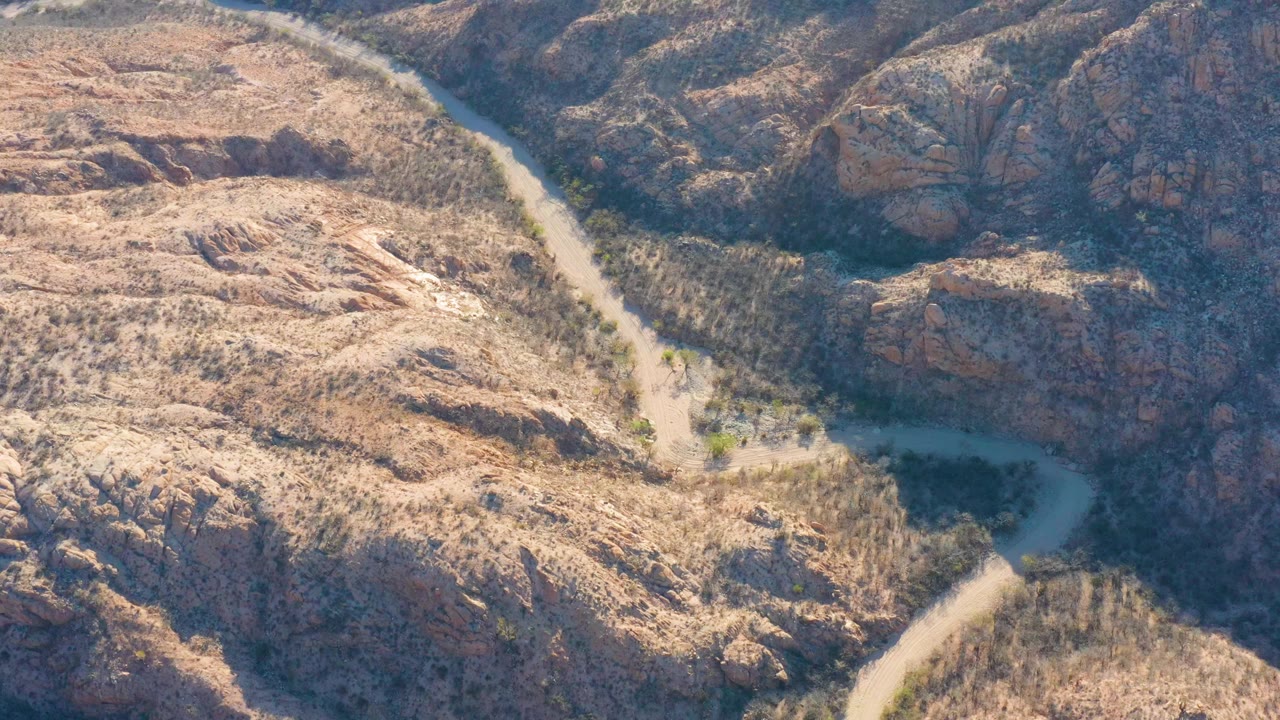Aerial frame over Cabo Pulmo, Baja California Sur showing a pale road curving through dry rocky hills with sparse scrub and no visible people.