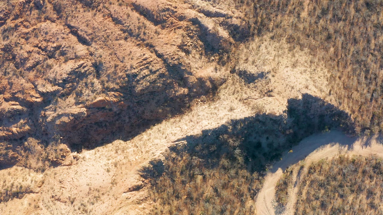 Rocky desert slope with a pale dirt path cutting through dry vegetation.