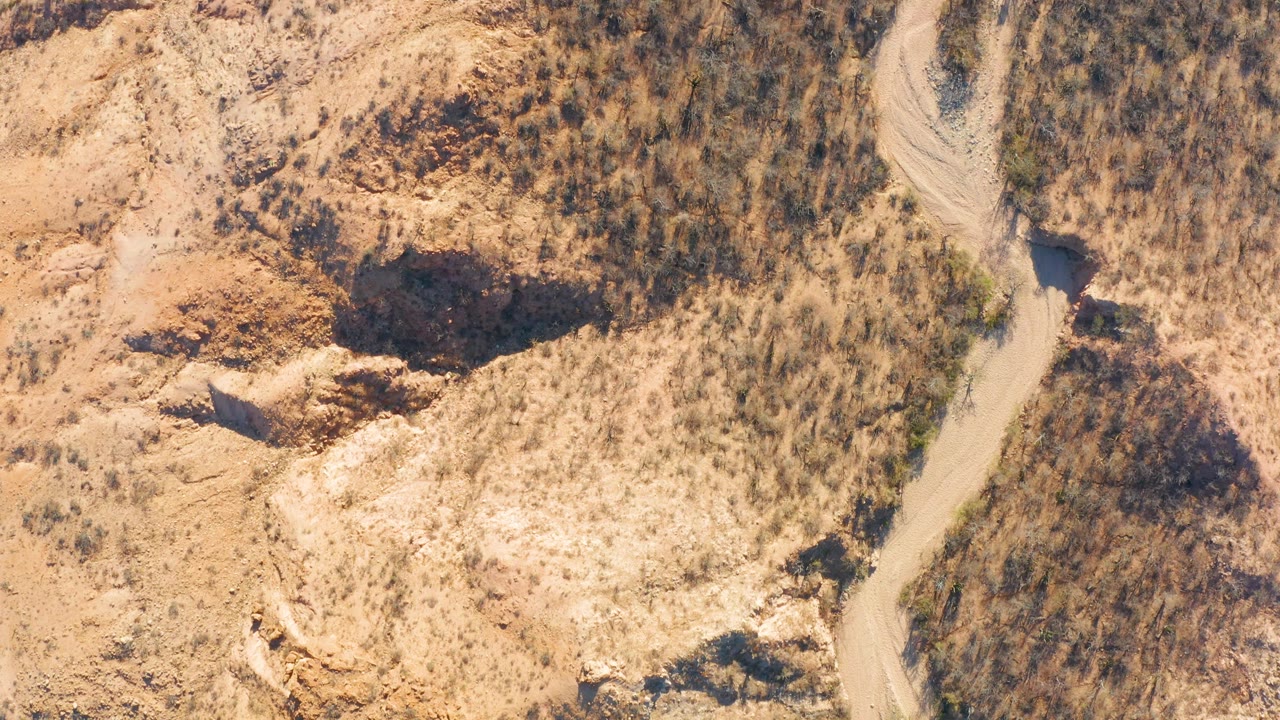 Aerial view of a dirt road bend beside scrub-covered hills.