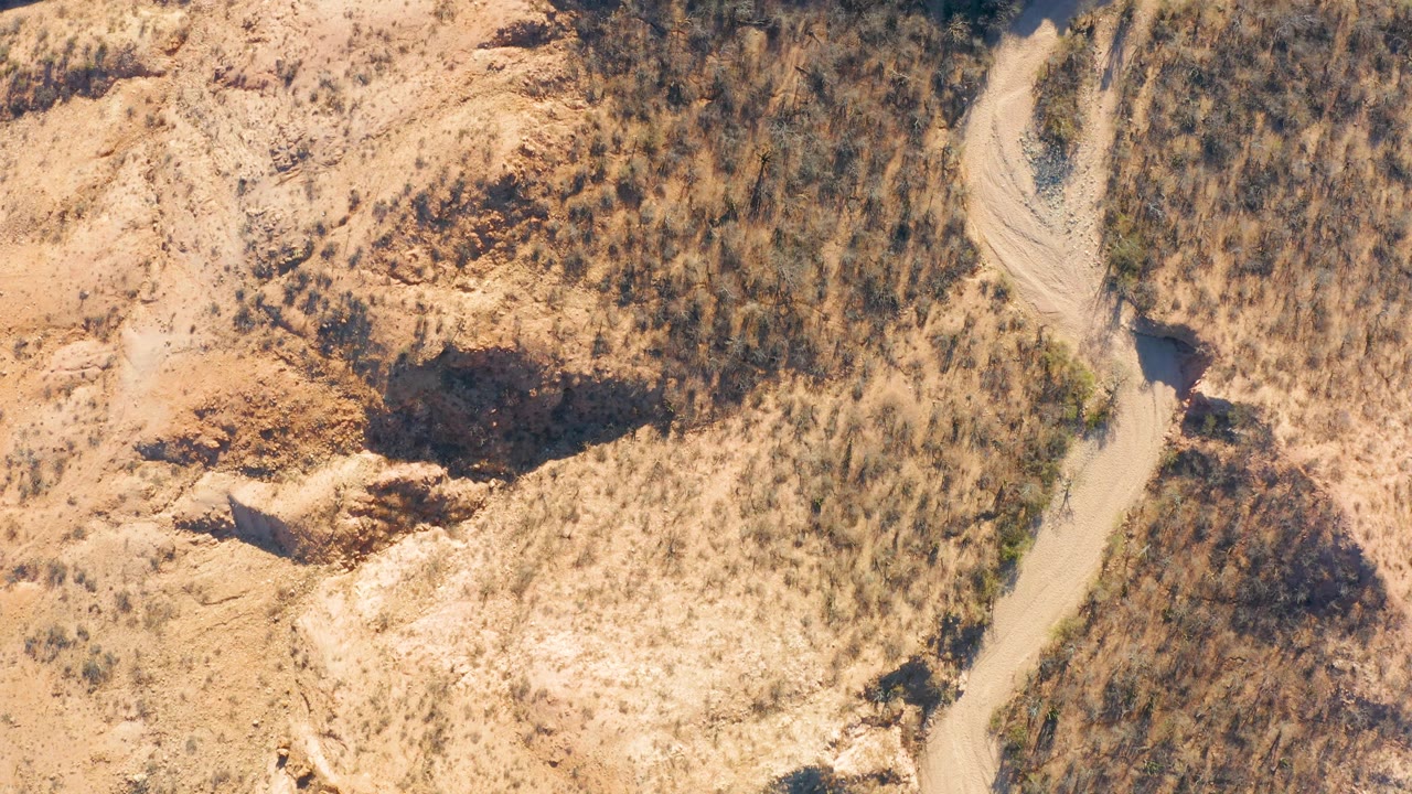 Top-down frame from Cabo Pulmo, Baja California Sur showing a dirt track threading through arid brush, tan soil, and rugged rock outcrops, with no visible people.
