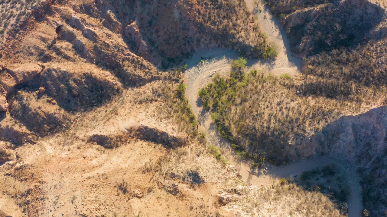 Aerial frame from Cabo Pulmo, Baja California Sur with the road bend near the upper center, dry grasses across the middle, rocky tan ground, and no visible people.