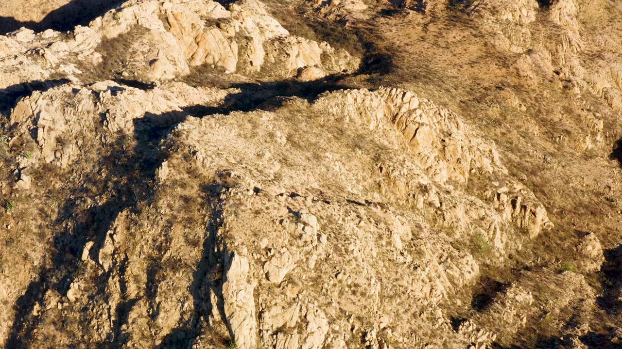 One second in, the view holds on pale rocky ridges and dry brush in Cabo Pulmo, Baja California Sur, with shadow pockets along the left side and no visible people.