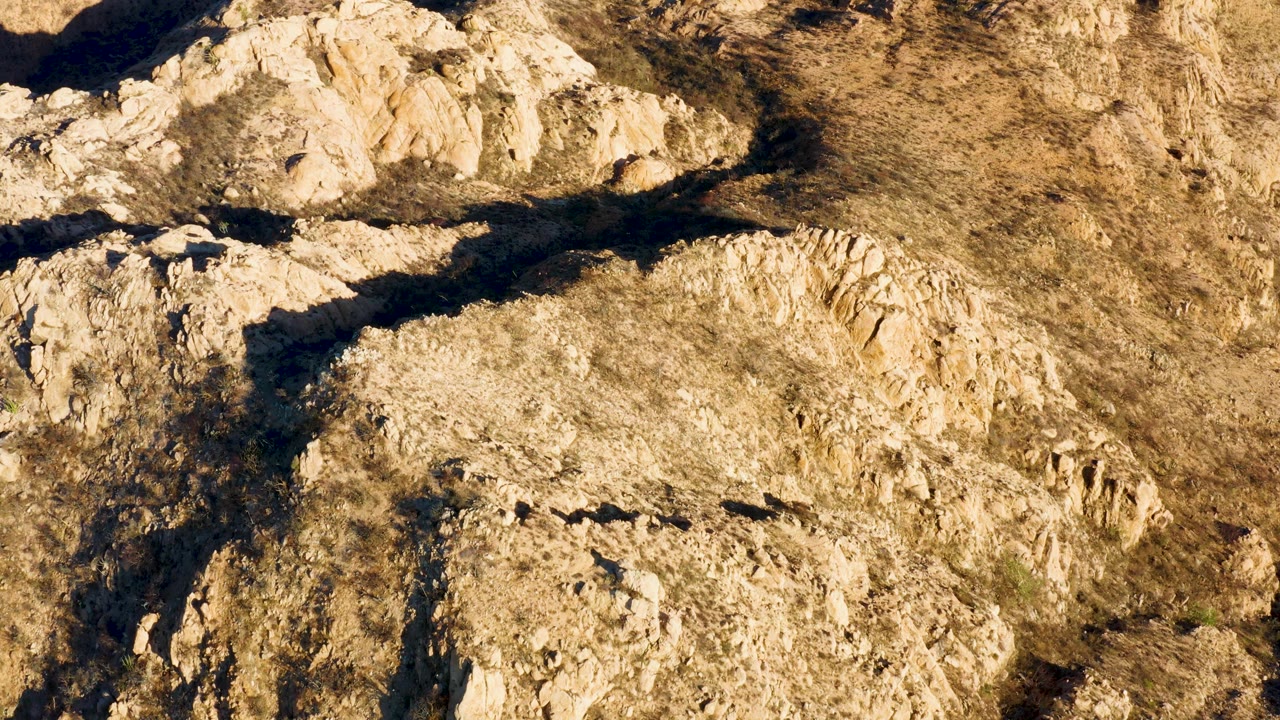 Midway through, arid rock shelves and tawny brush fill the Cabo Pulmo frame, with a broad shadow band crossing the upper rocks and no visible people.