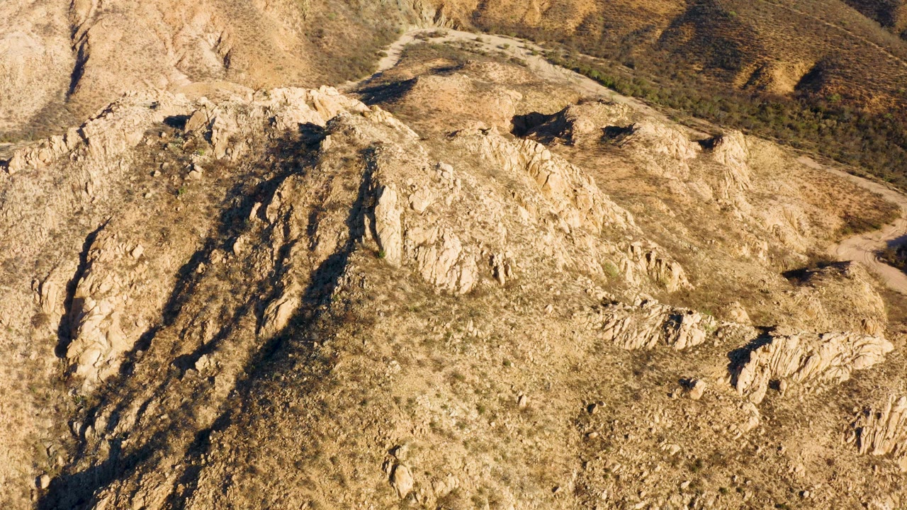 Aerial view over tan rocks, dry brush, and a curving road