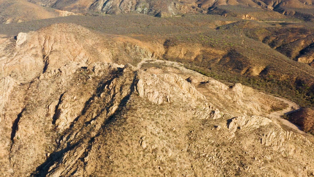 Arid mountain ridge with gullies, rock outcrops, and a dirt road beside it.