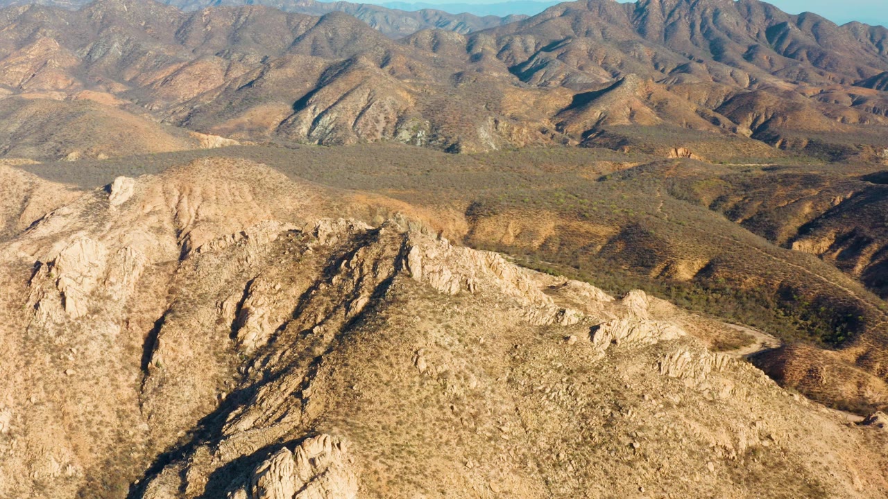 Cabo Pulmo mountain landscape with the foreground ridge lower in frame, a broad scrub-covered valley crossing the middle, distant rugged peaks, and no visible people.