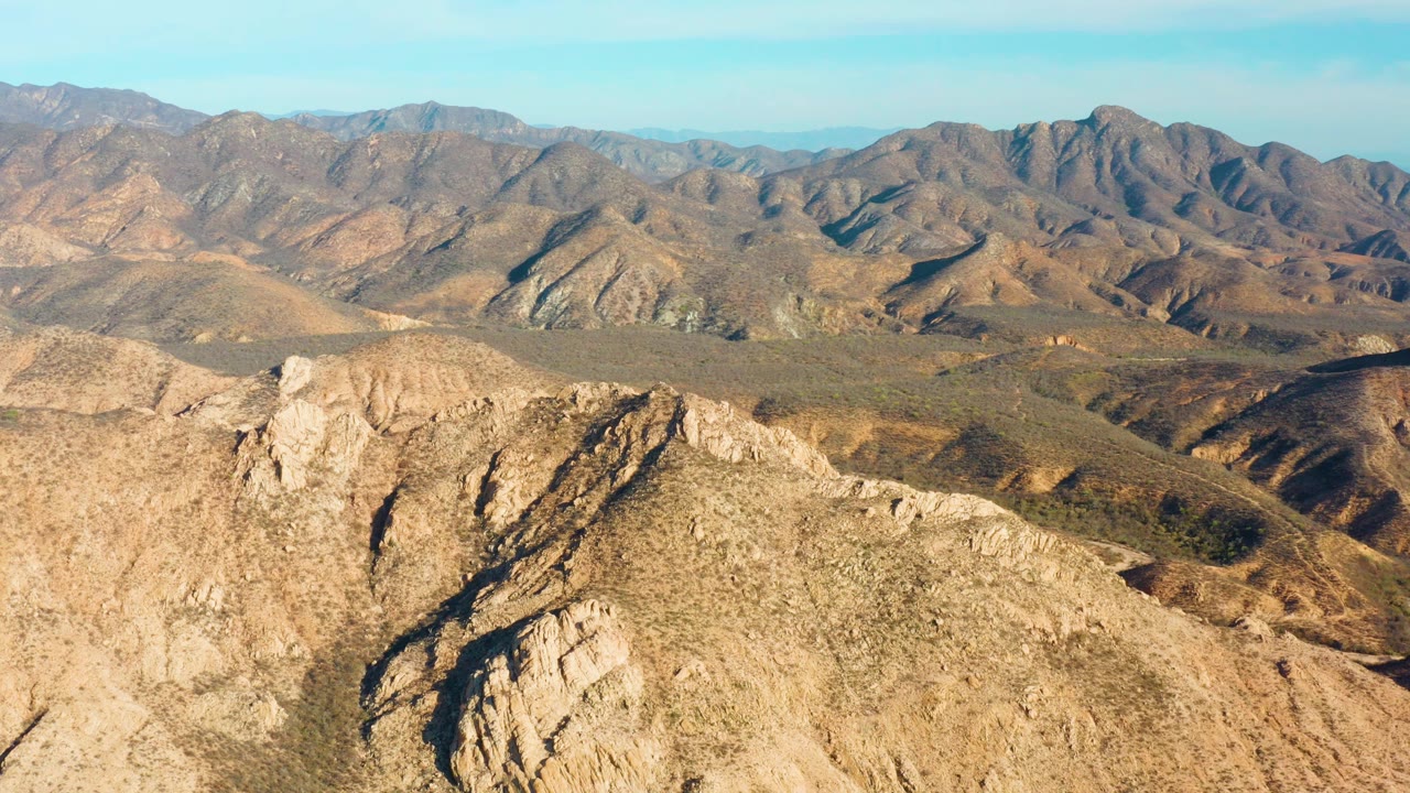 Aerial view of dry rocky mountains under a clear blue sky.