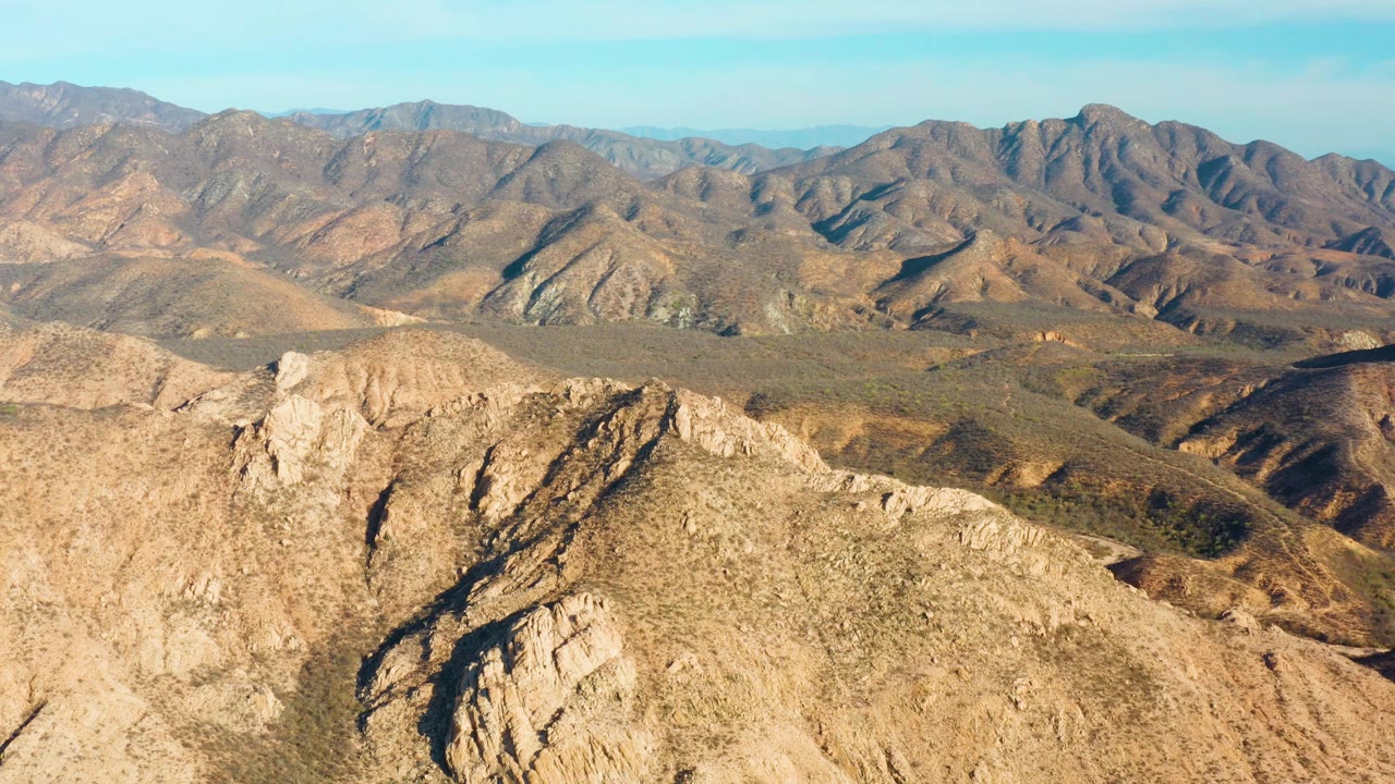 Cabo Pulmo aerial frame with a pale rock outcrop filling the lower foreground, brown ridges across the middle distance, blue sky above, and no visible people.